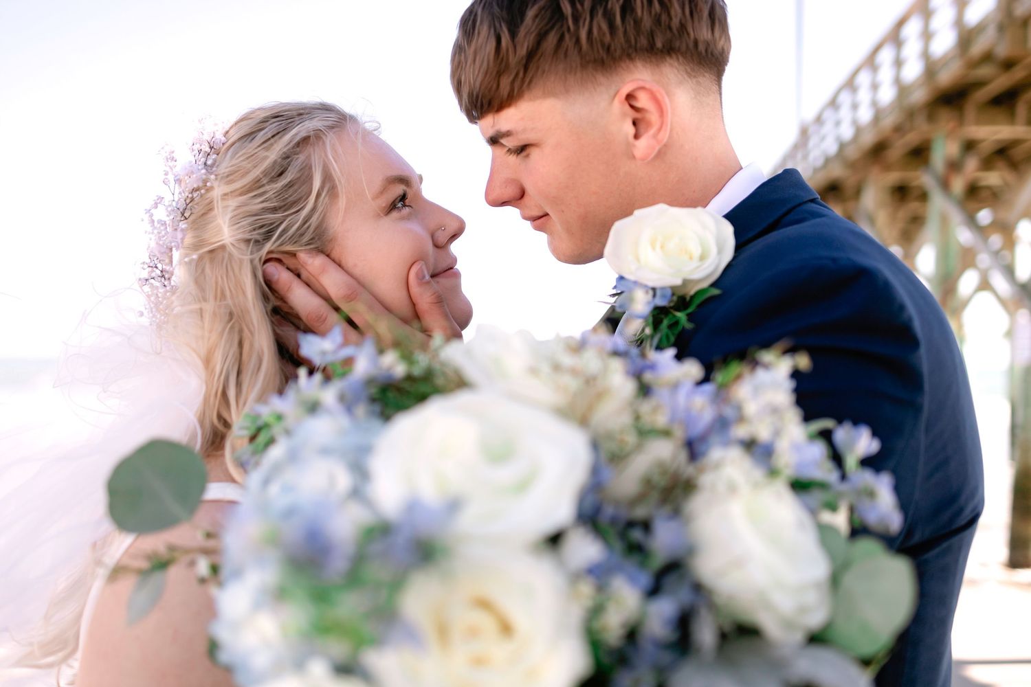 Close-up of bride and groom nearly kissing with a bouquet of white and blue flowers in the foreground.