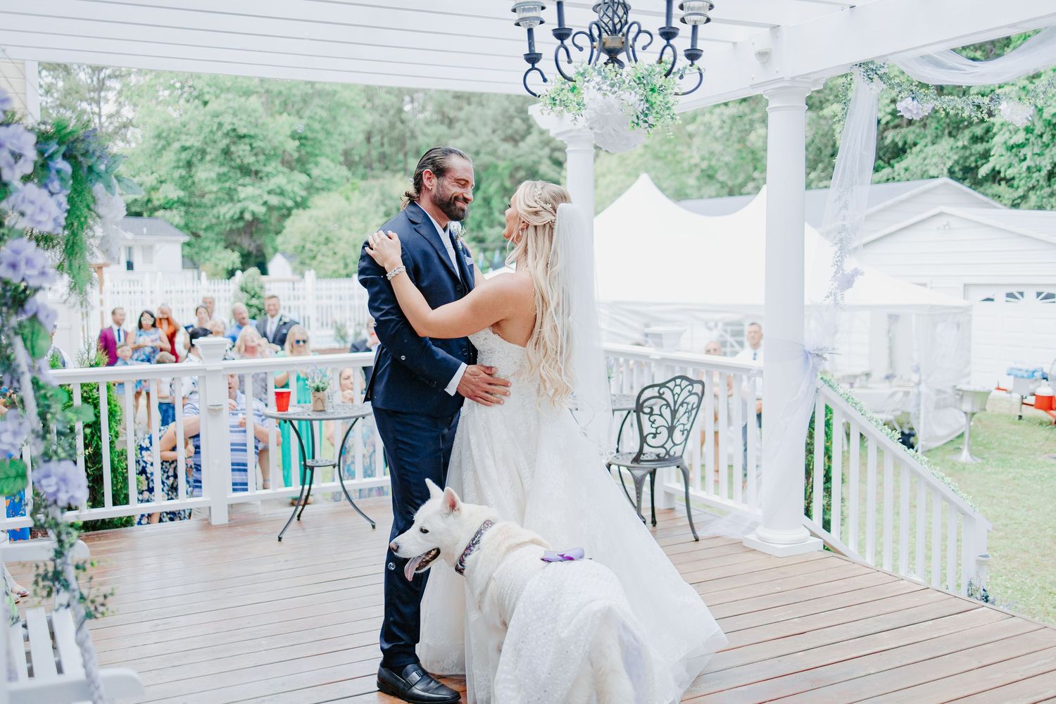 Bride and groom share first dance on decorated outdoor porch with white dog joining the celebration.