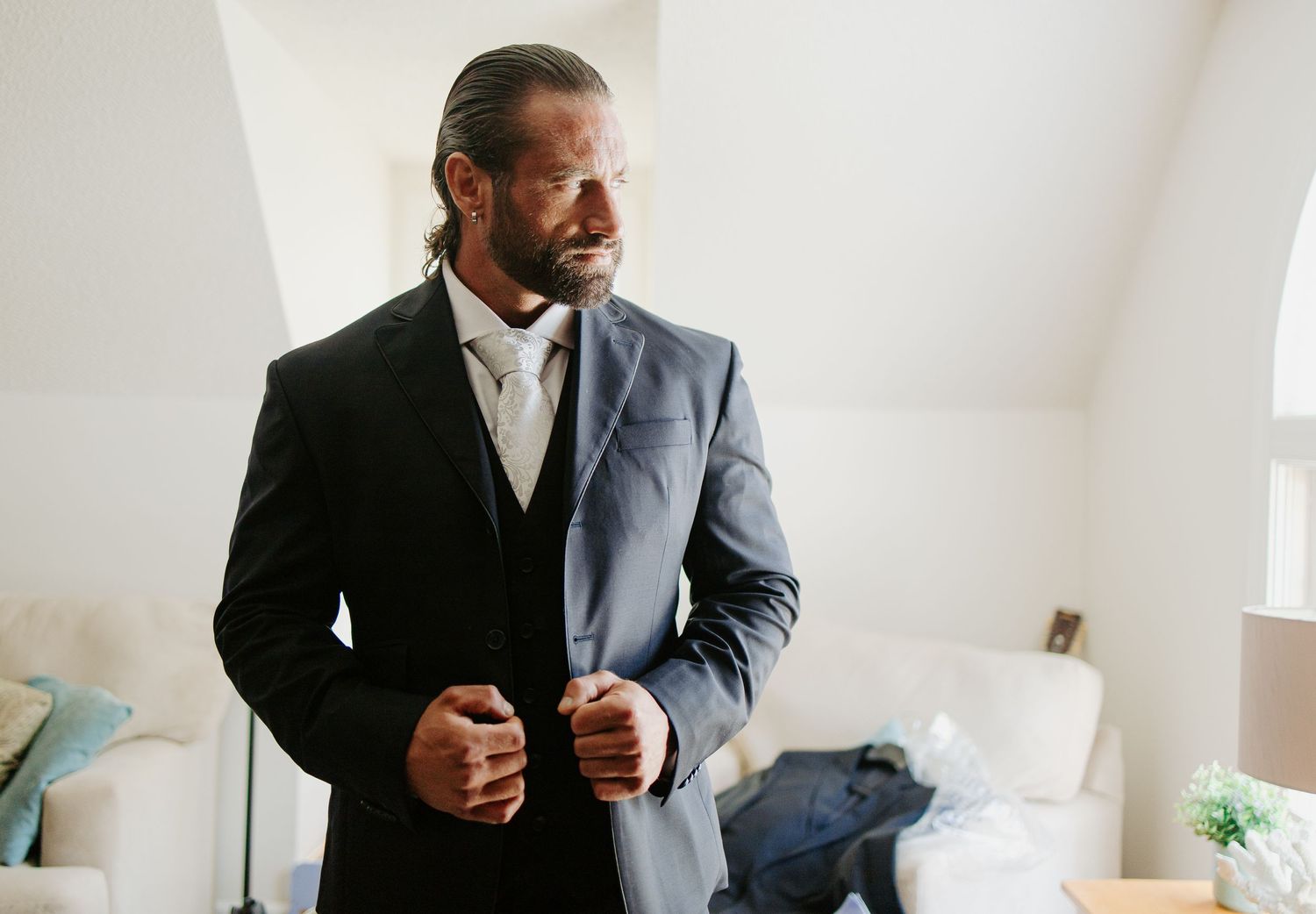 Groom in a charcoal suit buttoning his jacket while preparing for his wedding ceremony.