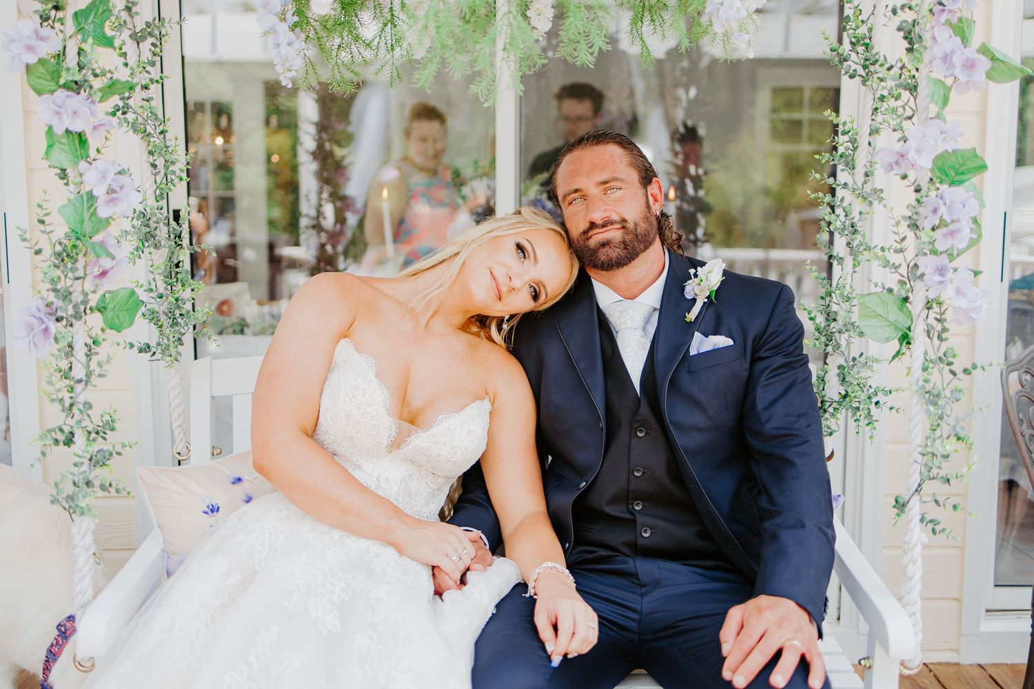Bride and groom sit together on swing surrounded by hanging wisteria flowers at elegant wedding venue.