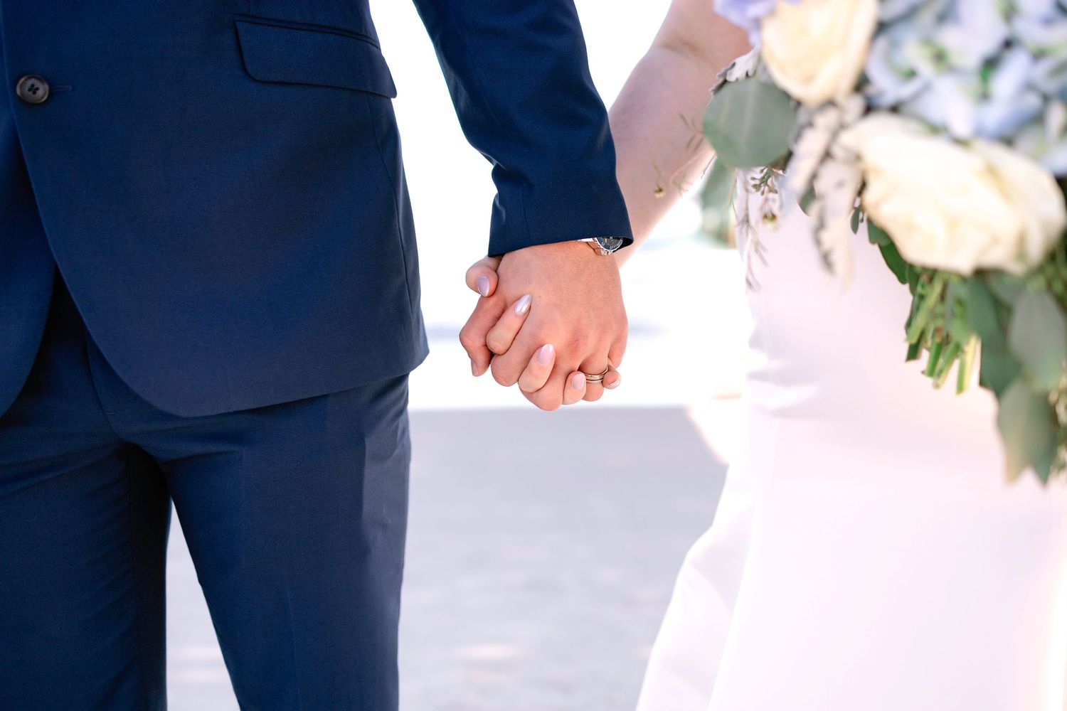 Close-up of bride and groom holding hands near a white floral arrangement during their wedding ceremony.