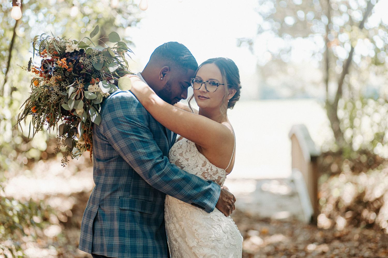 Newlyweds share tender moment outdoors with rustic autumn floral bouquet.