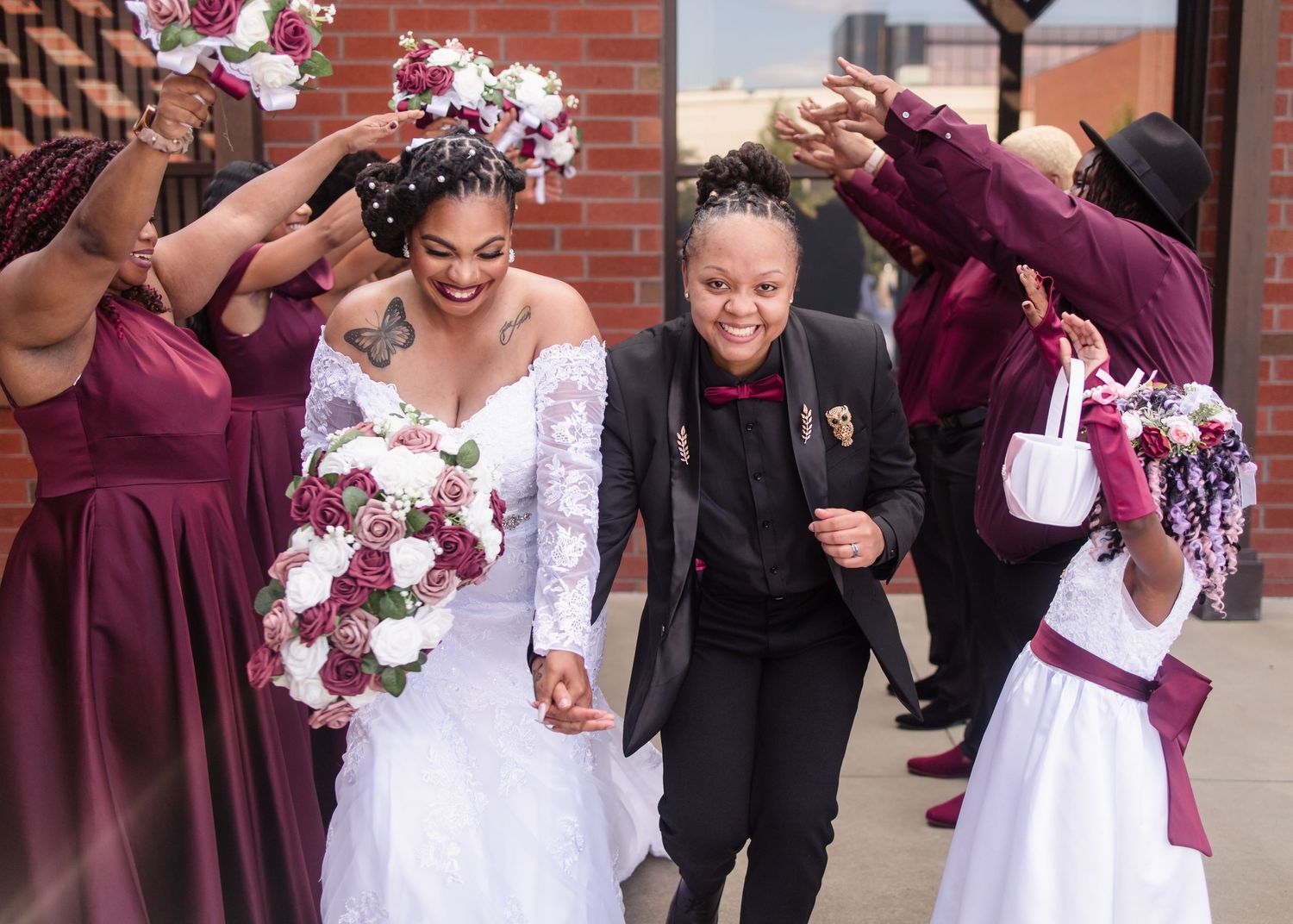 A bride in a white lace gown walks with bridesmaids in burgundy dresses at her wedding.