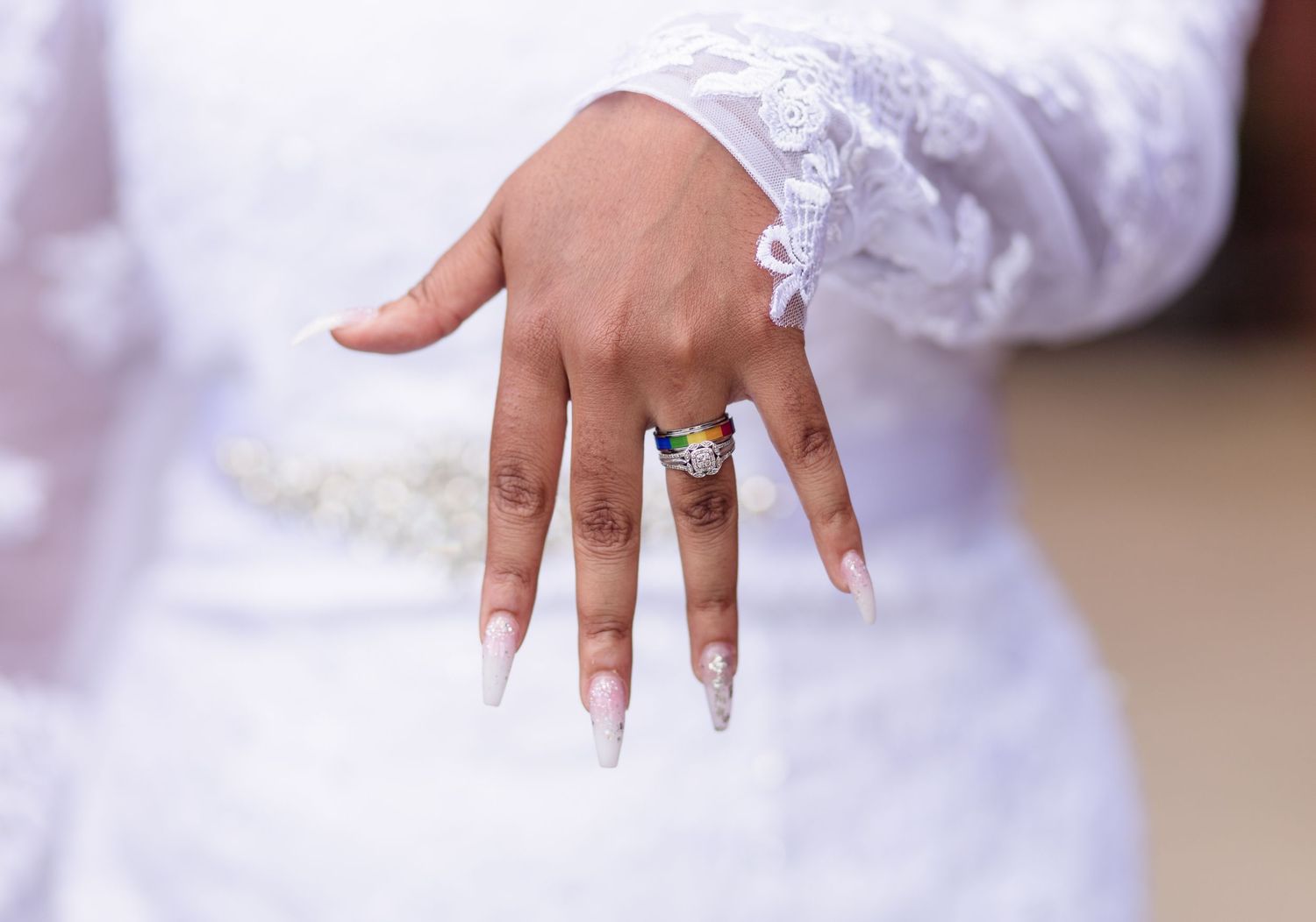 Close-up of a bride's hand displaying a colorful gemstone ring with long white manicured nails.