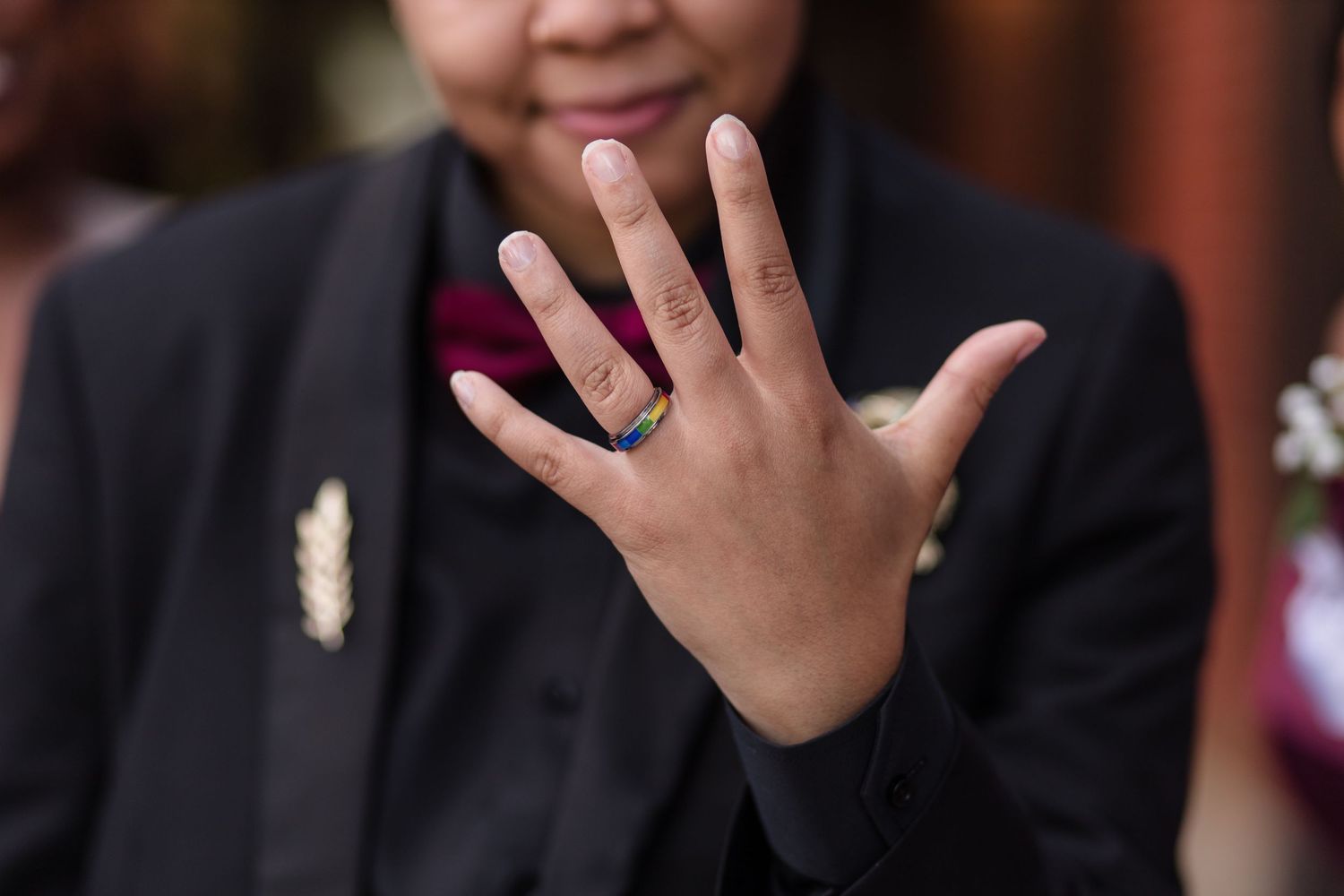 Close-up of a hand wearing a gold wedding band against a black suit jacket background.