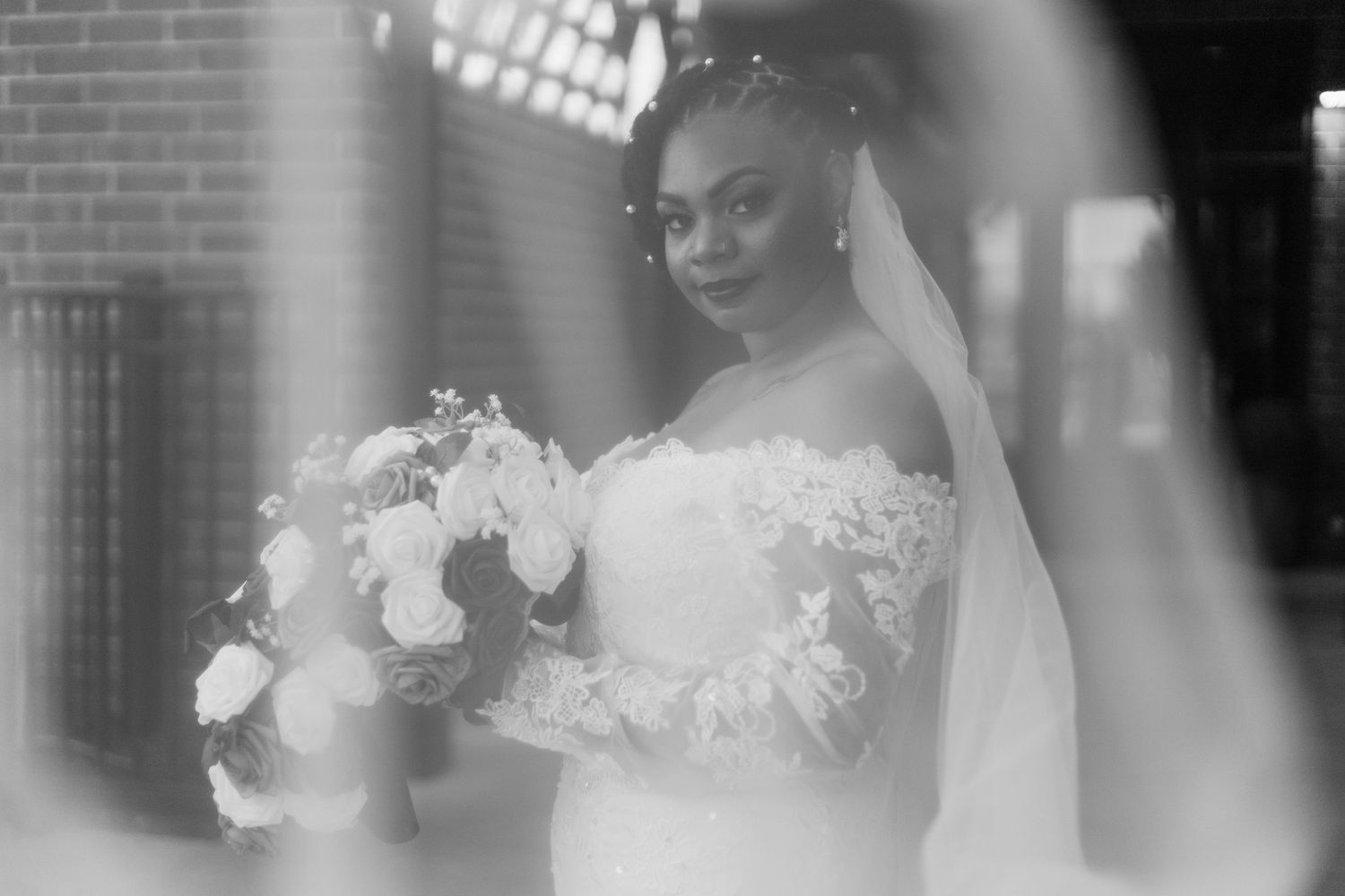 Black and white portrait of a bride in a white gown and veil holding a bouquet in soft light.