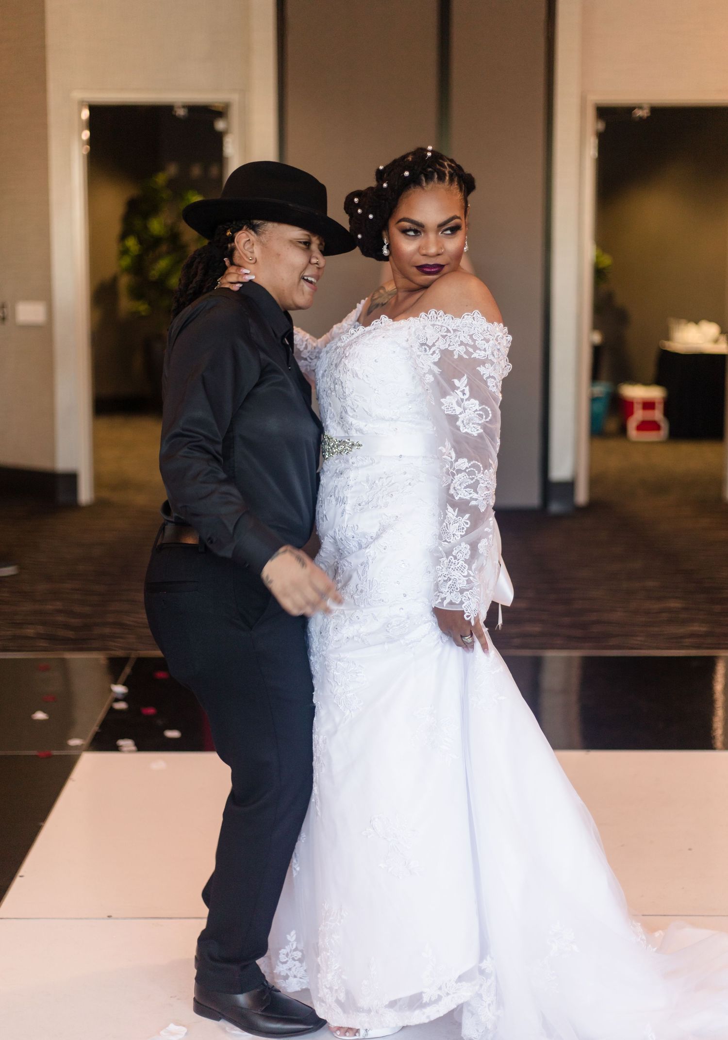 Two brides pose and laugh together on dance floor at wedding reception.