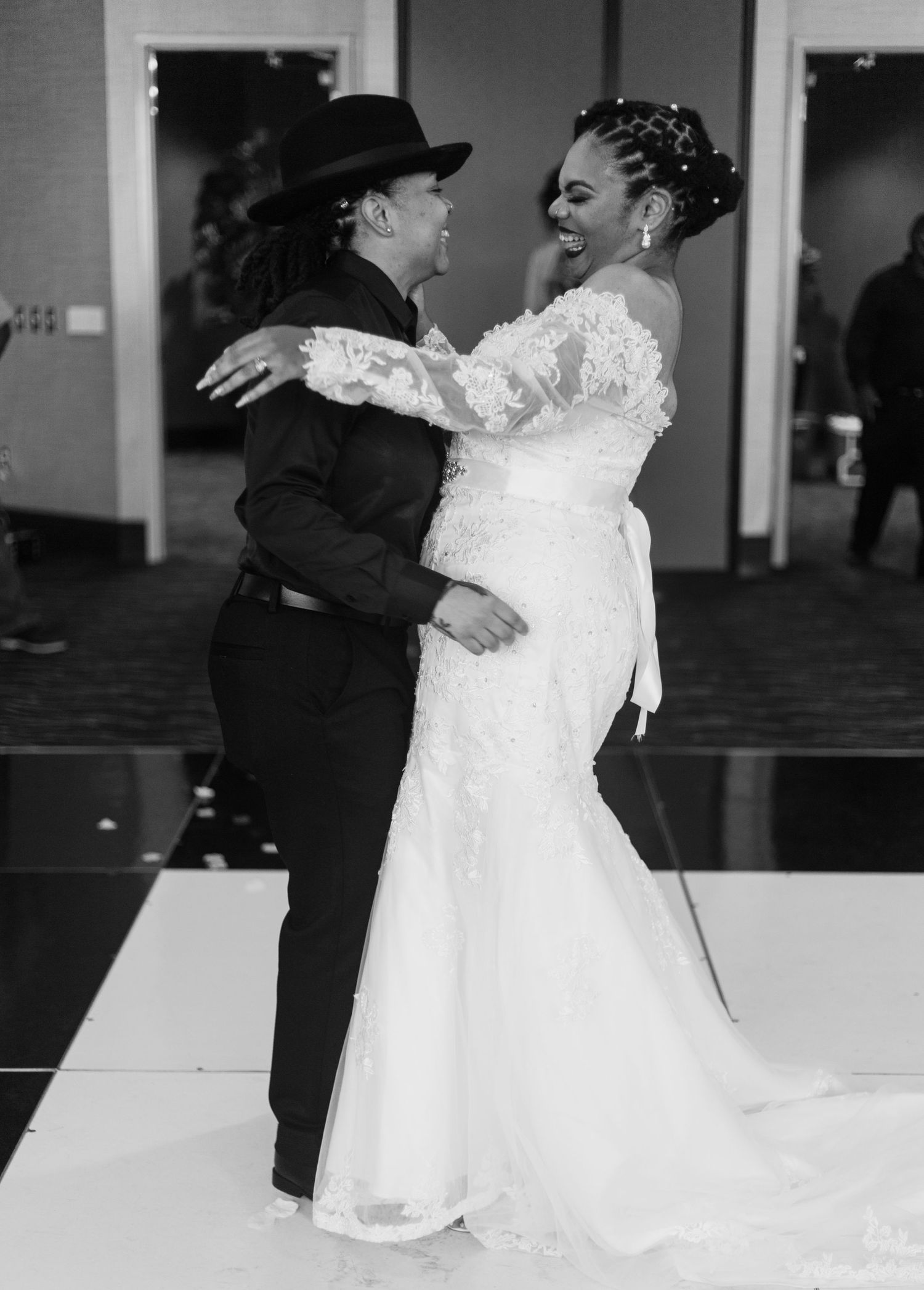 Black and white photo of two brides laughing and dancing at their wedding.