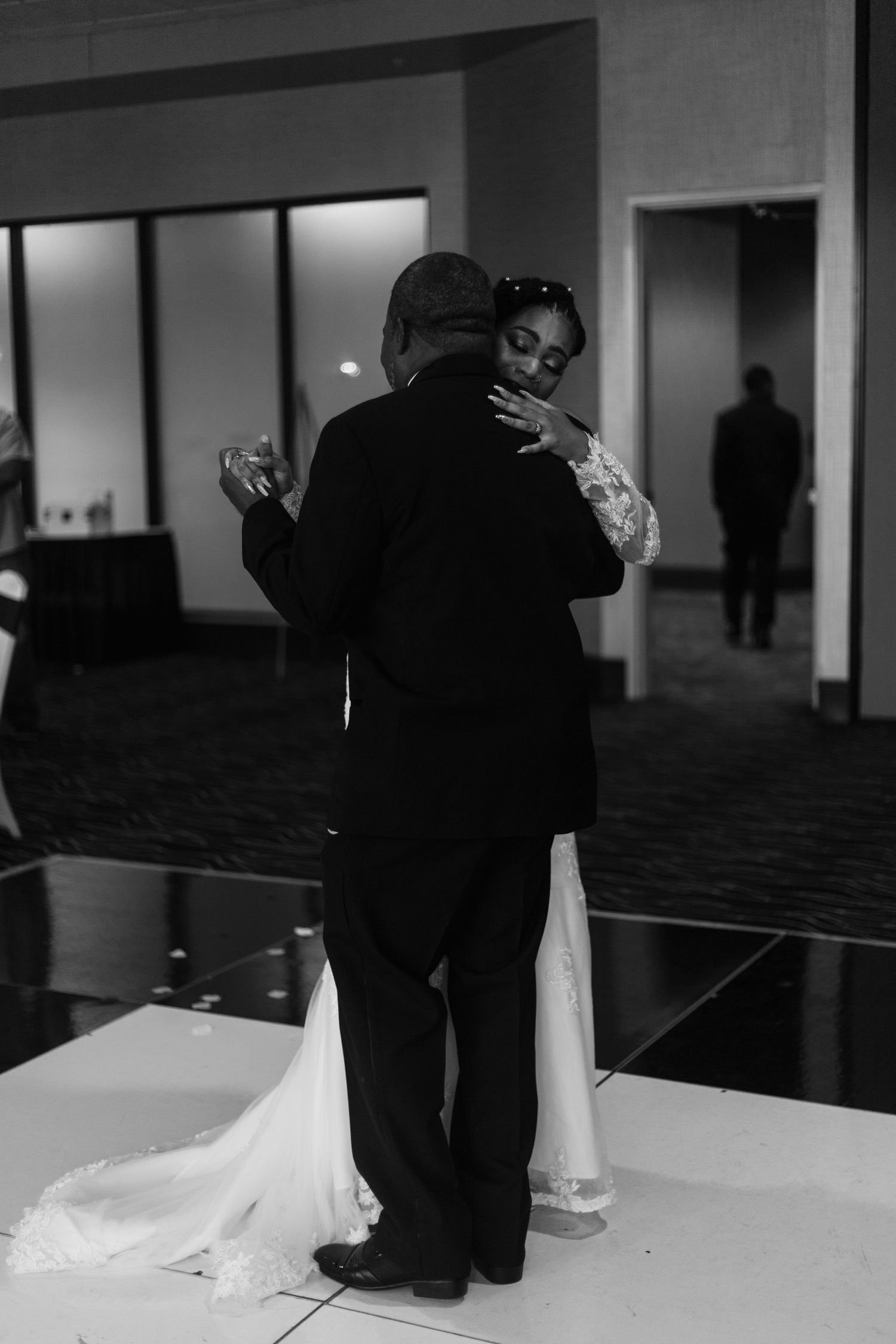 Bride and partner share emotional slow dance on white dance floor at reception.