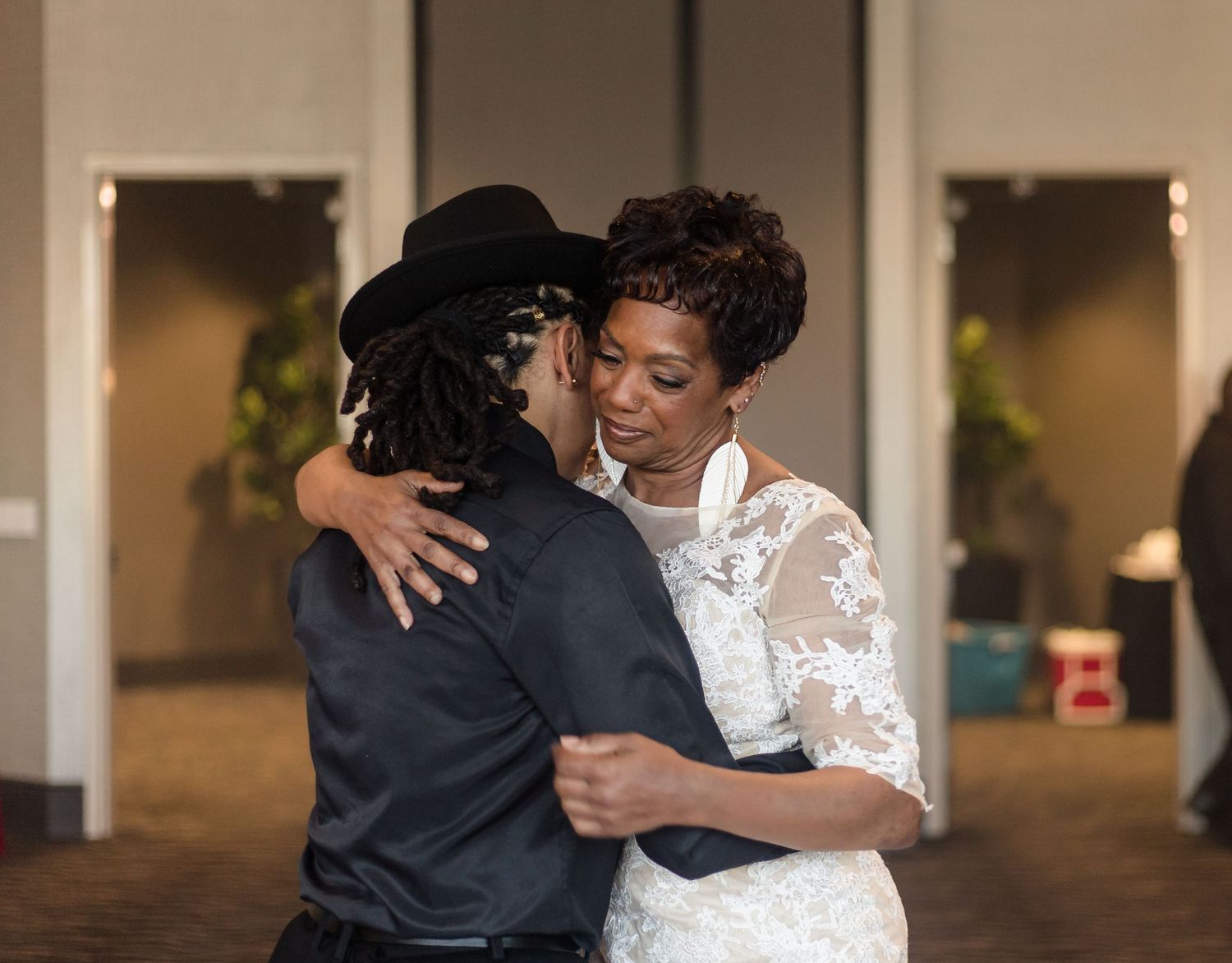 Two women share a tender embrace while dancing at a wedding reception in an elegant venue.