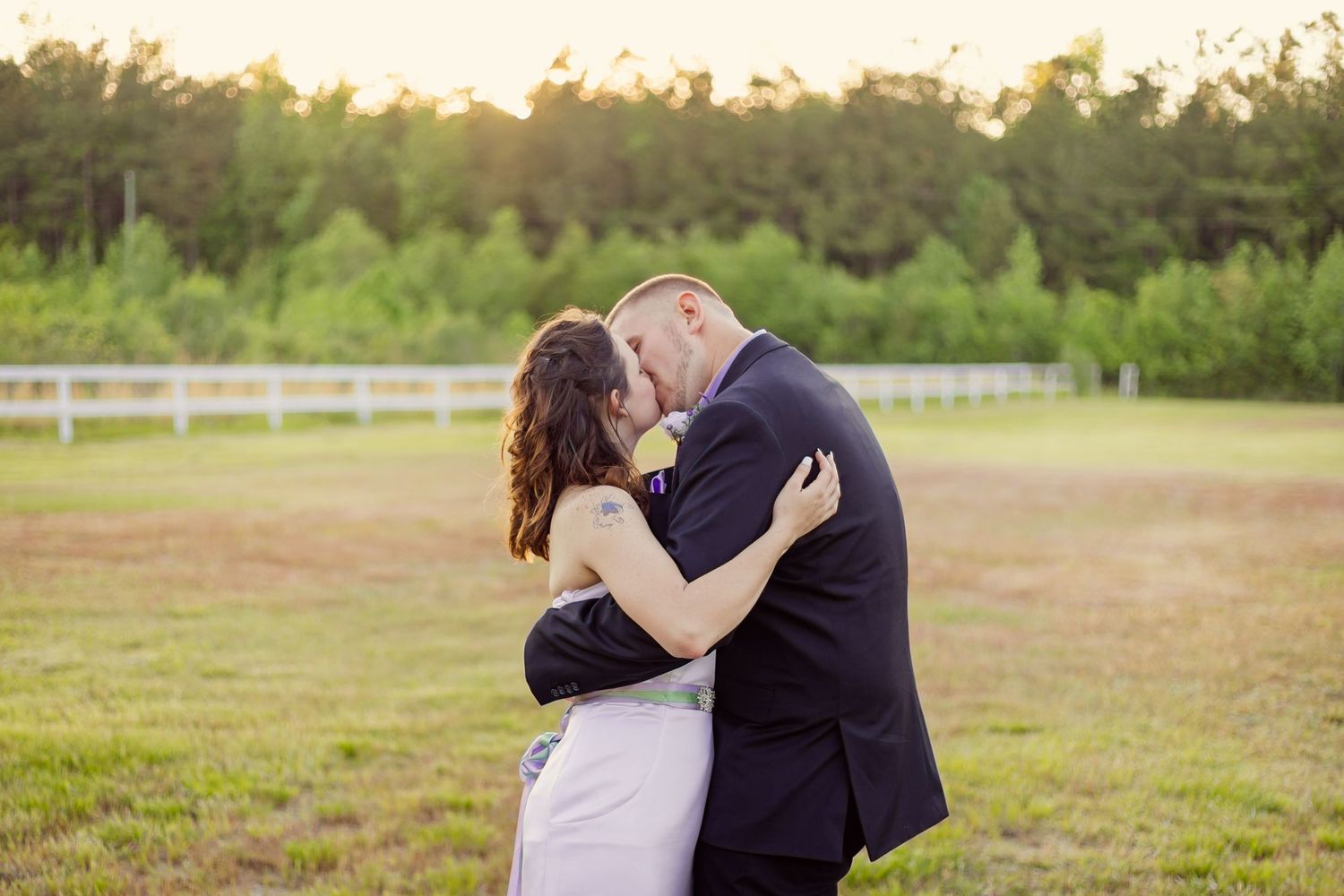 Bride and groom share a tender forehead-to-forehead moment in a lush green field at sunset.