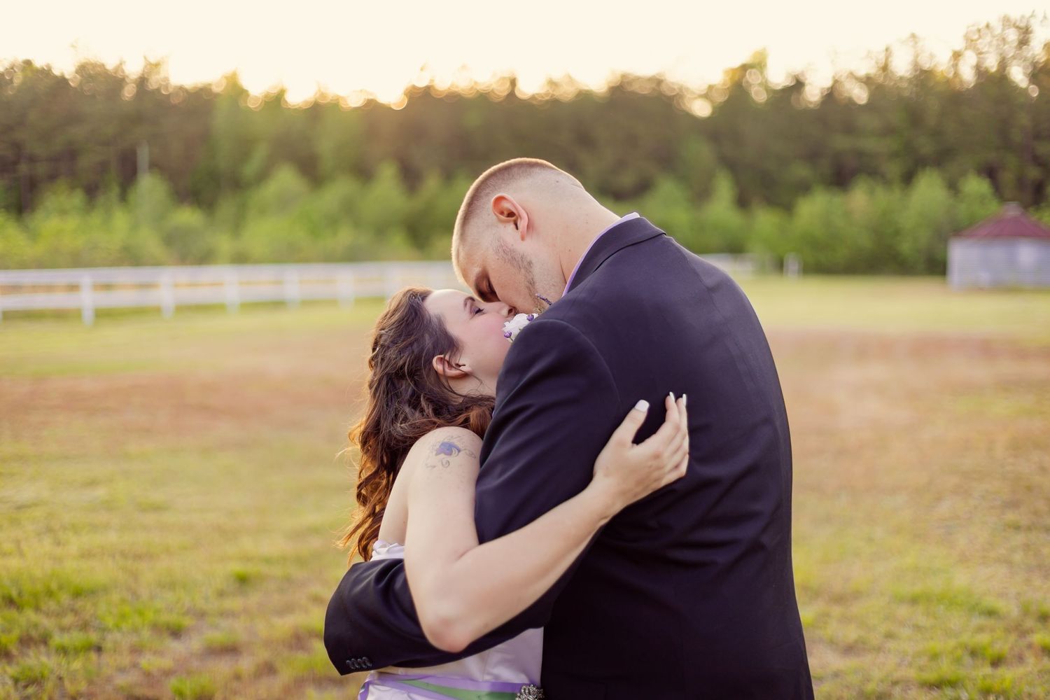 Wedding couple shares a passionate kiss in an open green field during golden hour photography.