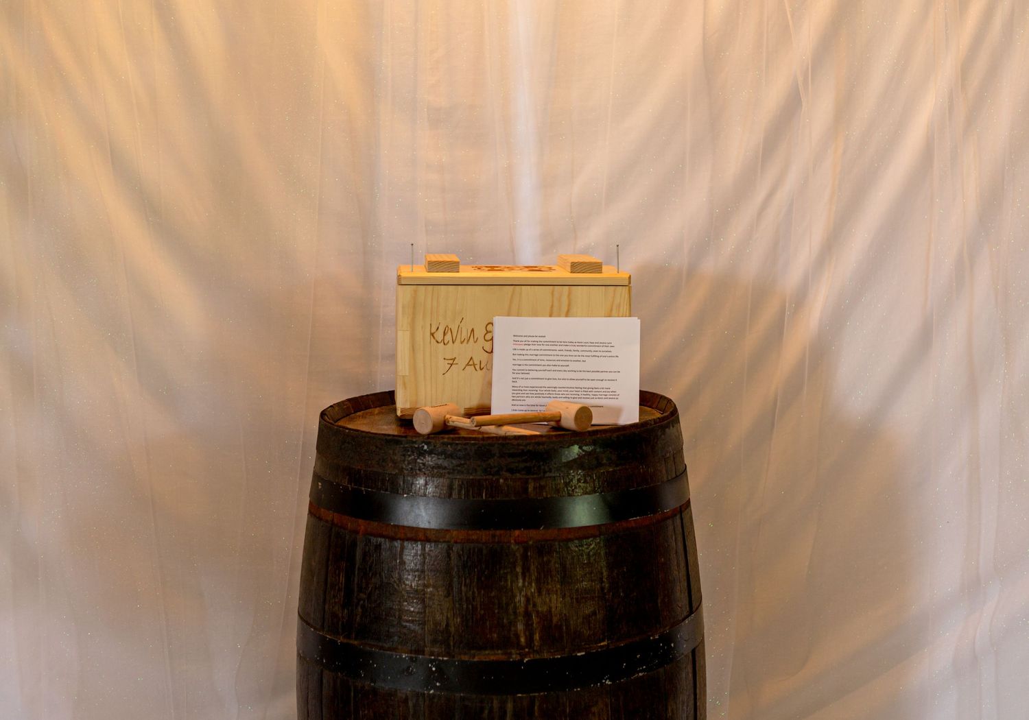 Rustic wooden box on vintage wine barrel against white draping at wedding venue.
