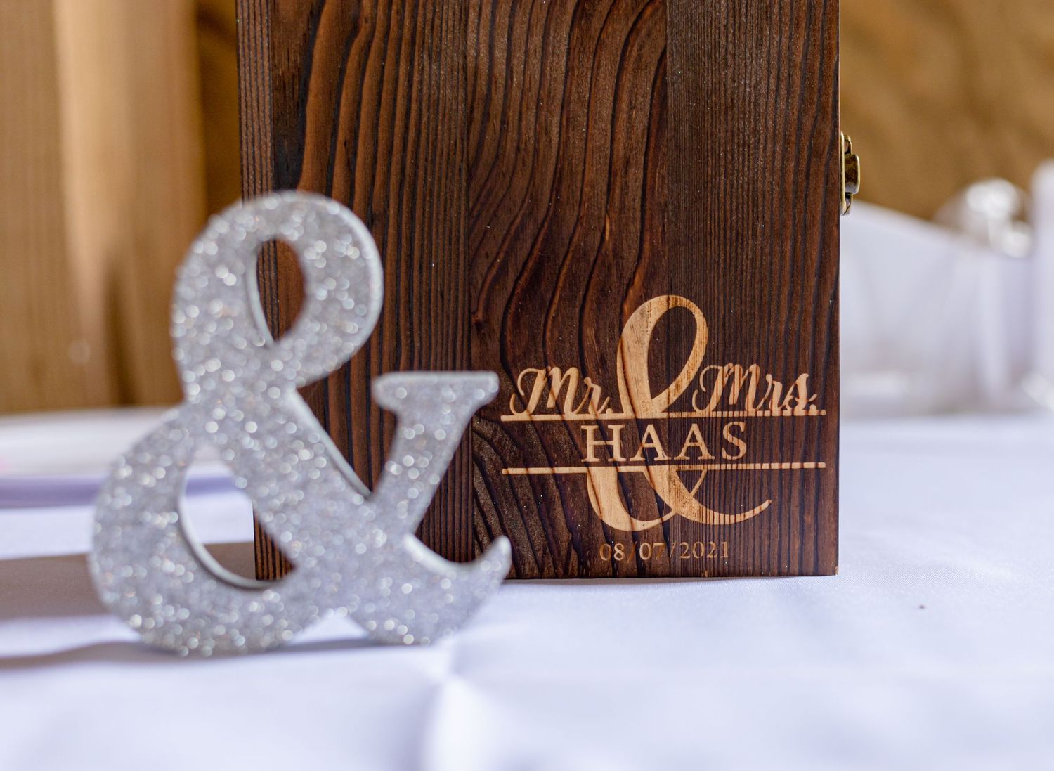 Engraved wooden Mr. and Mrs. Haas wedding box with glitter ampersand sign on white table.