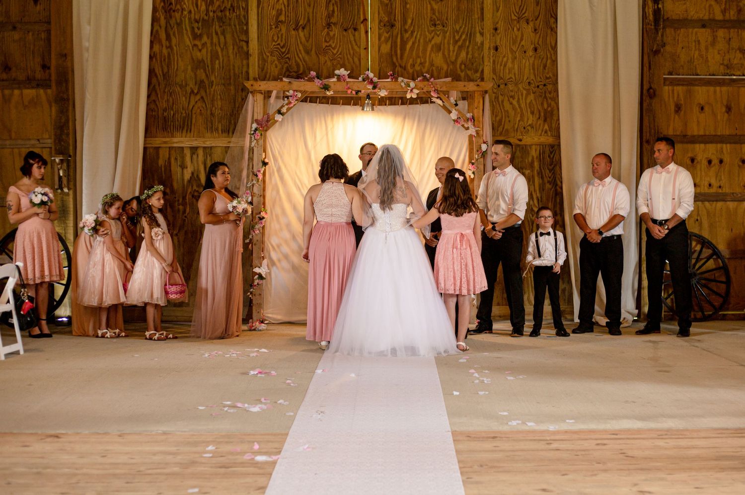 Bride walking down the aisle in a barn wedding venue with pink floral arch.