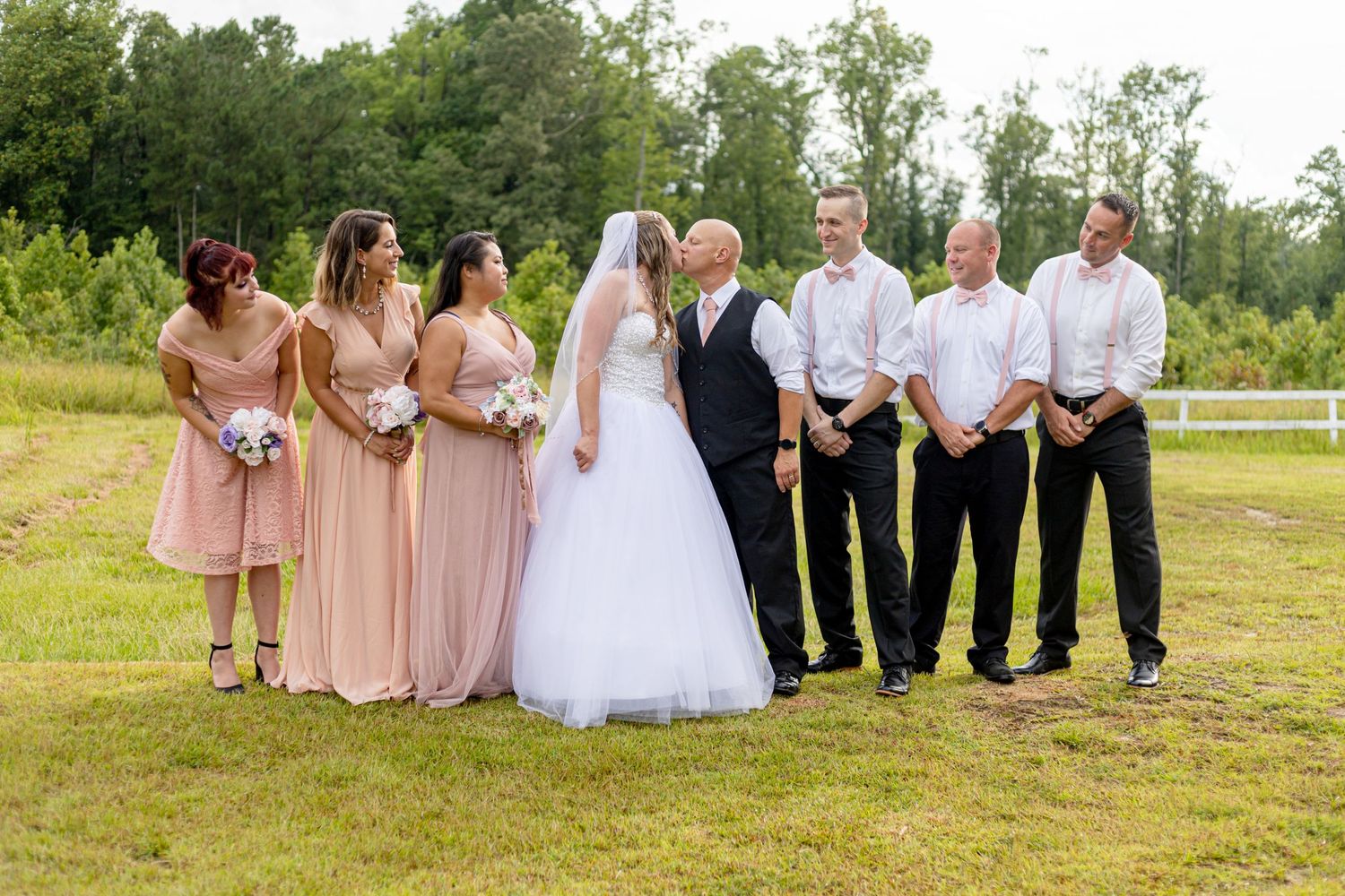 Wedding party standing together outdoors with bridesmaids in blush pink and groomsmen in white.