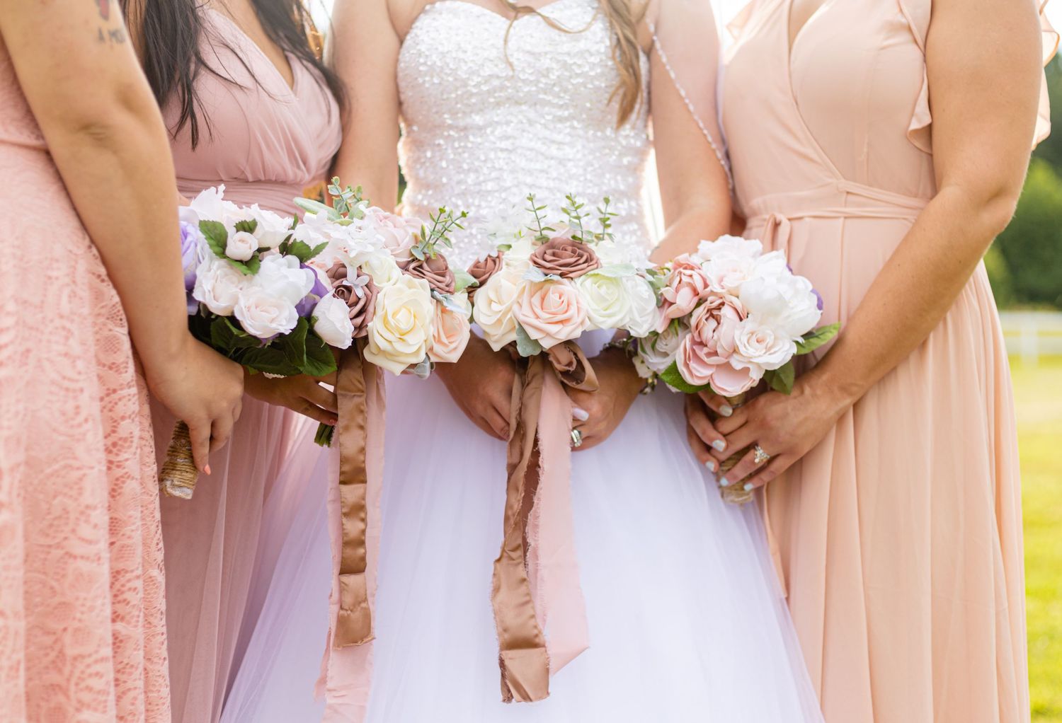 Bride and bridesmaids in blush pink dresses holding elegant floral bouquets outdoors.