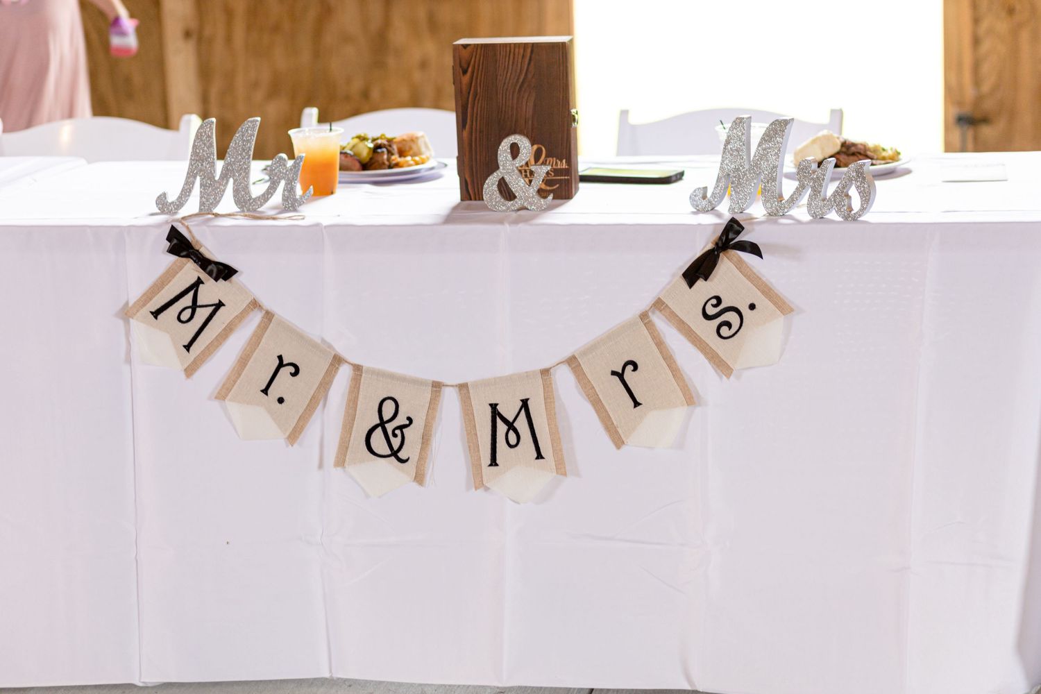 Mr. and Mrs. burlap banner decorates a white tablecloth wedding reception head table.