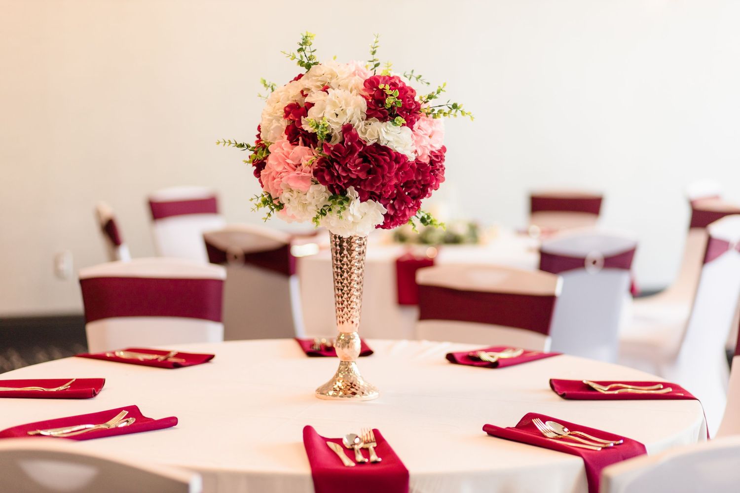 Elegant wedding reception table with tall pink and burgundy floral centerpiece and red napkins.