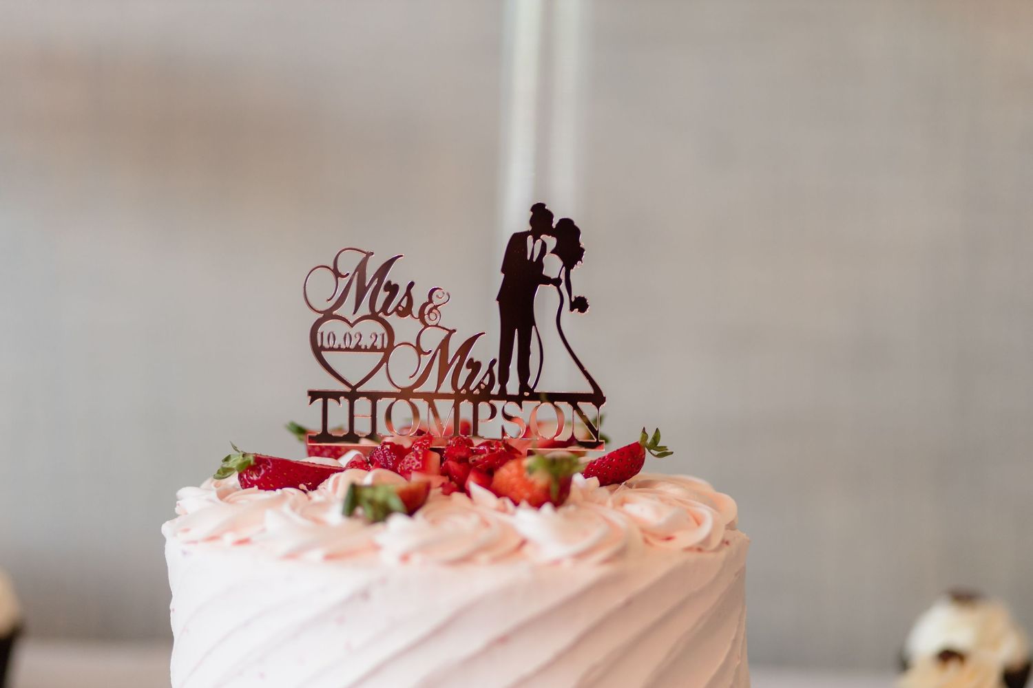 Elegant wedding cake topped with Mr. & Mrs. Thompson cake topper, adorned with fresh strawberries and pink frosting.