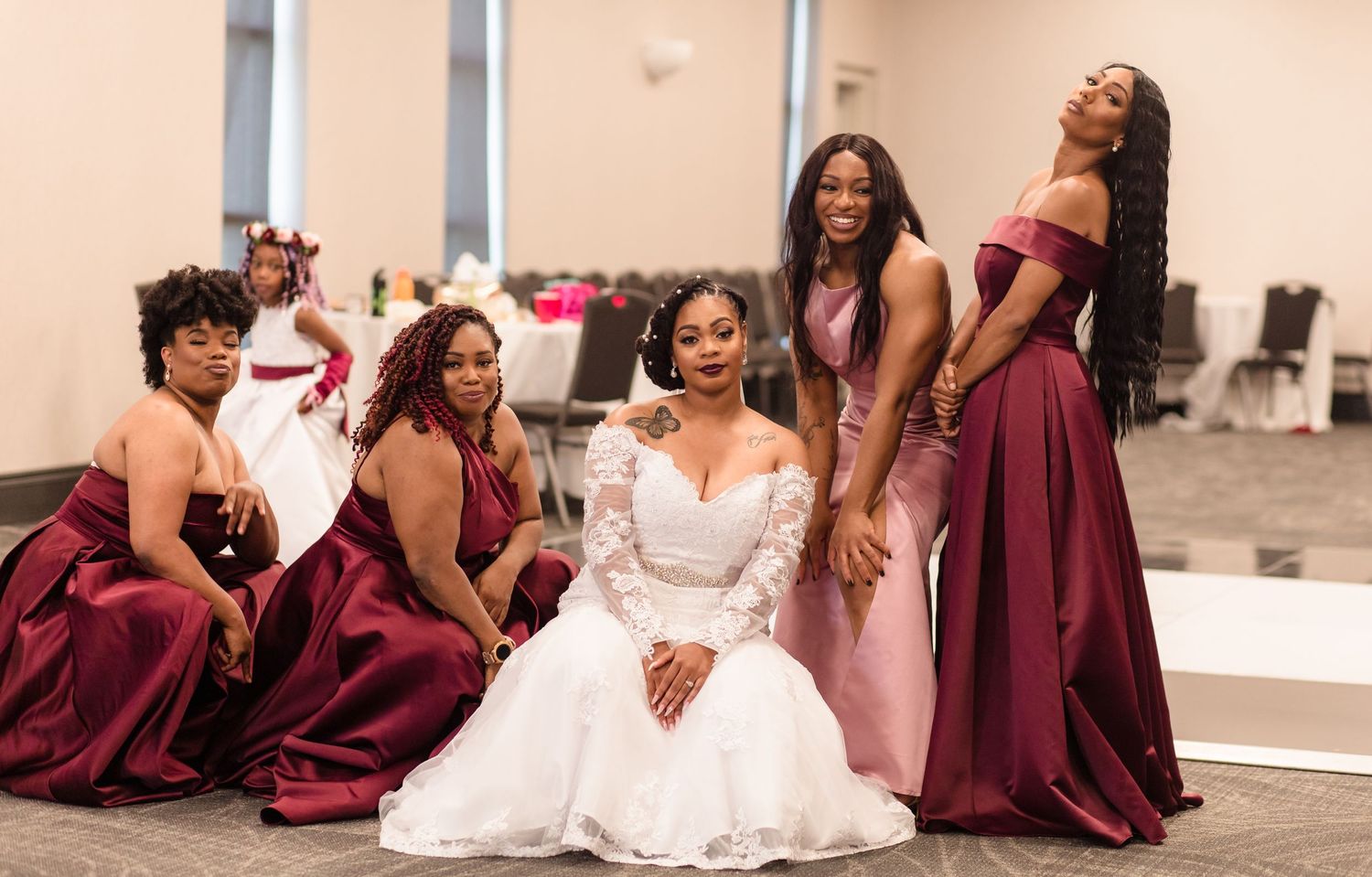 Bride in white gown surrounded by bridesmaids in burgundy and pink dresses posing together at wedding reception.