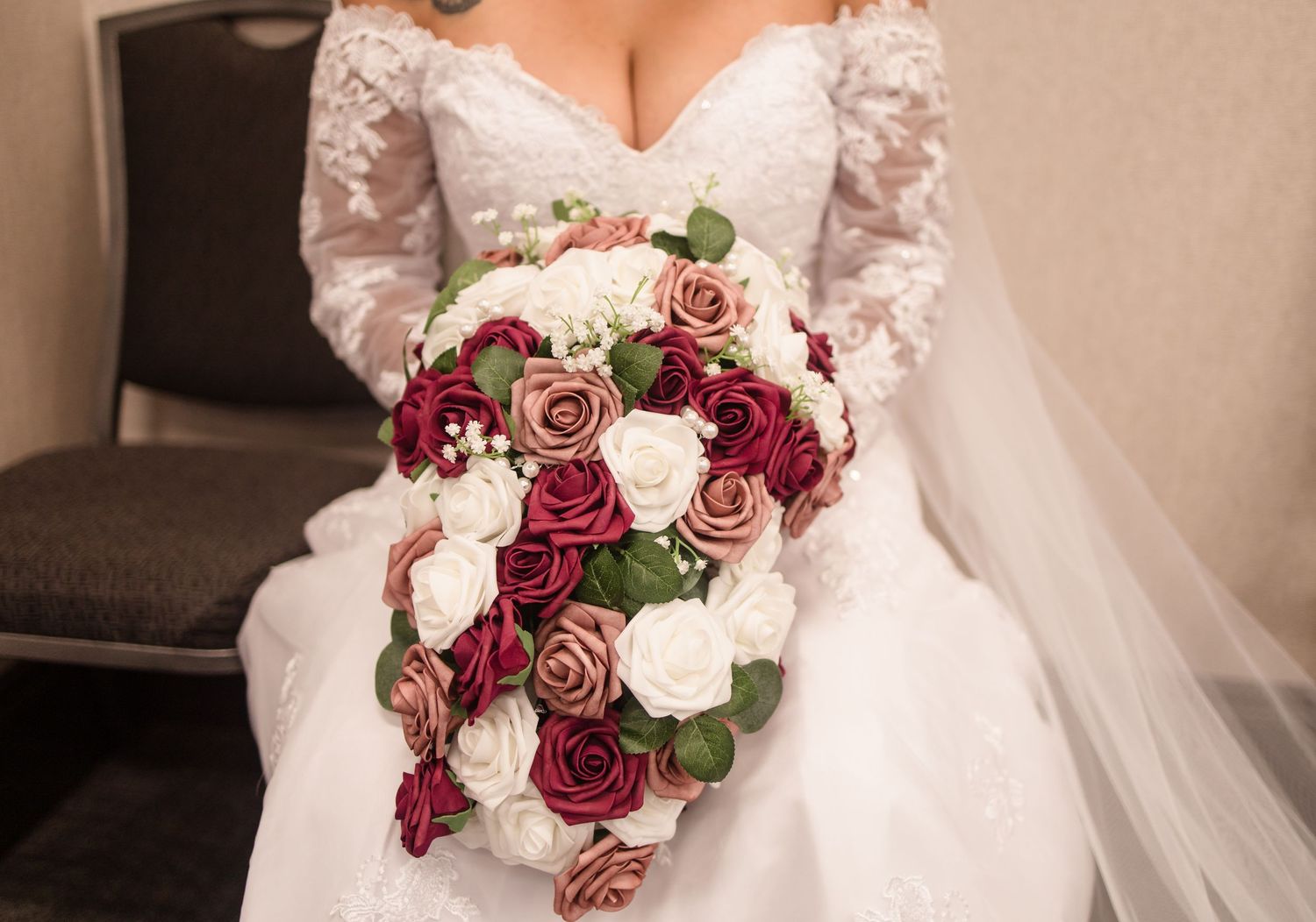 Bride holding stunning cascading bouquet of burgundy, pink, and white roses with greenery accents.