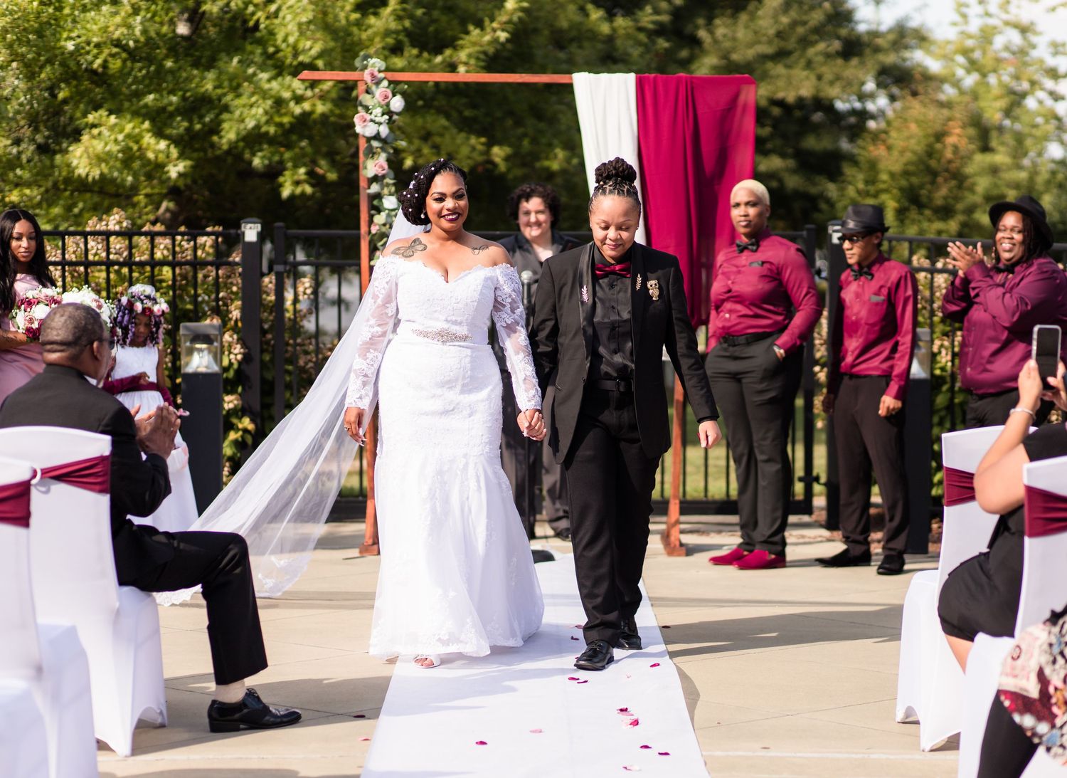Newlywed couple walking down the aisle after outdoor wedding ceremony with burgundy and white decorations.