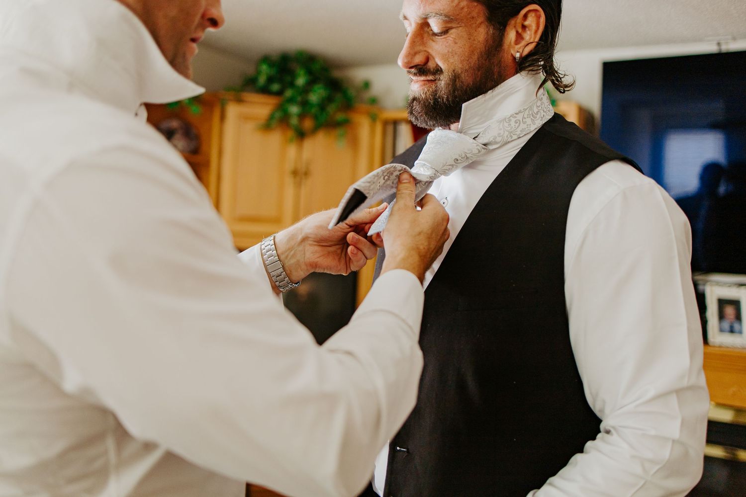 Groom getting his tie adjusted by a helper while preparing for his wedding day.