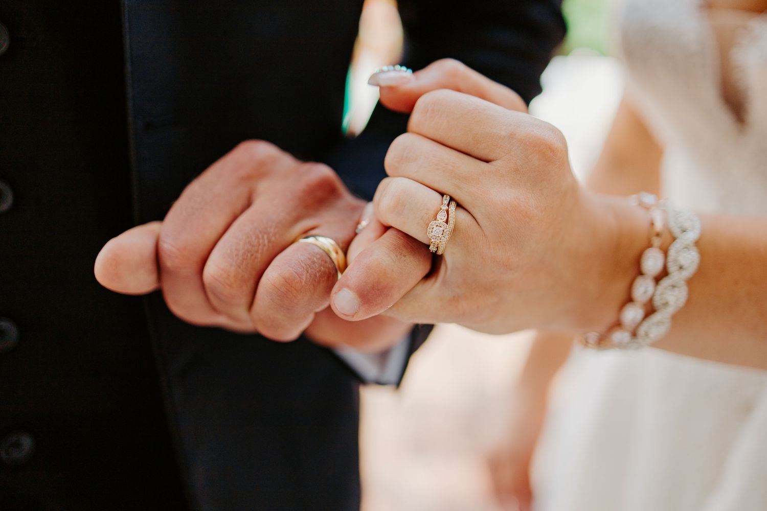 Close-up of bride and groom exchanging gold wedding rings with pearl bracelet detail.