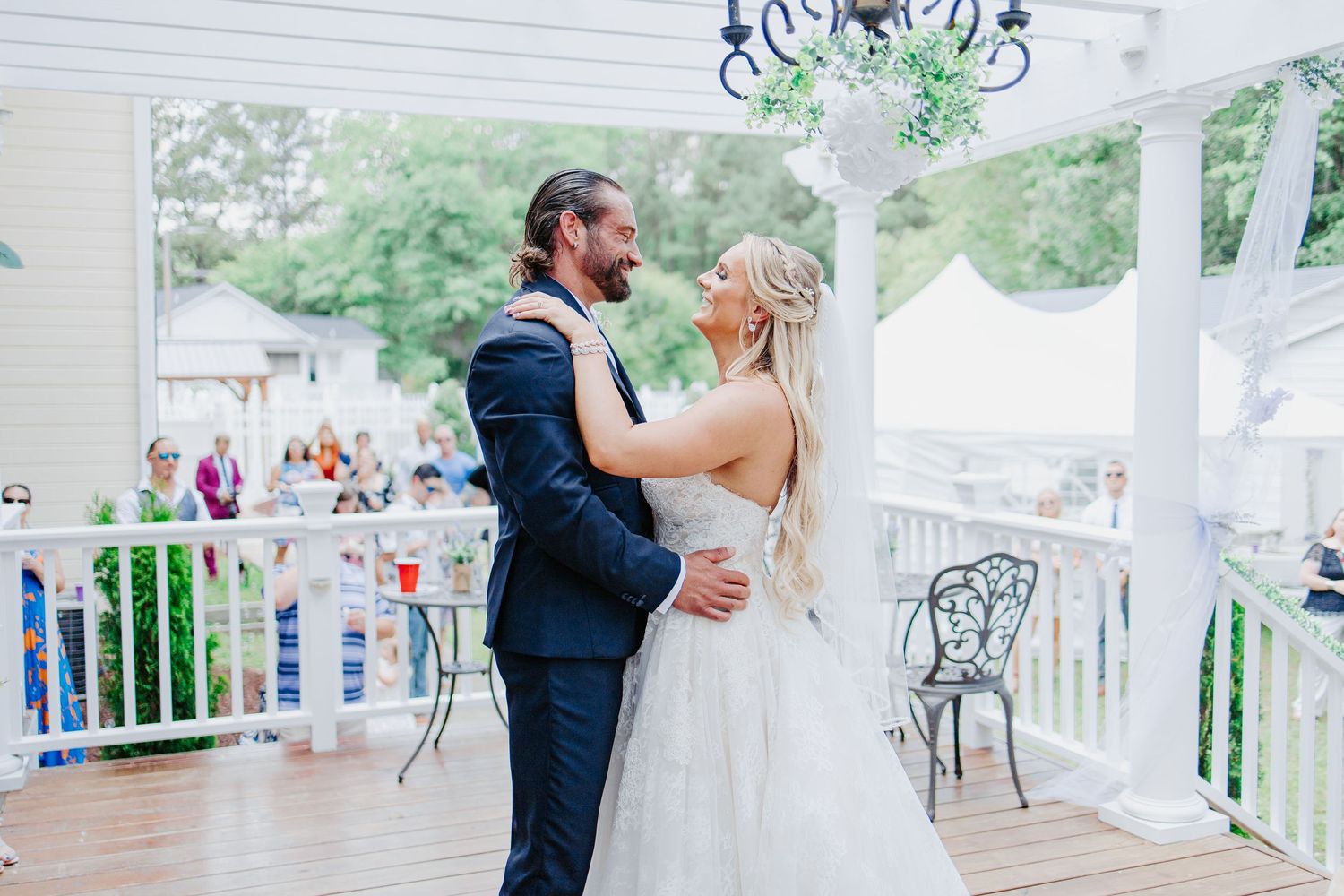 Bride and groom share romantic first dance on wooden outdoor porch surrounded by lush greenery.