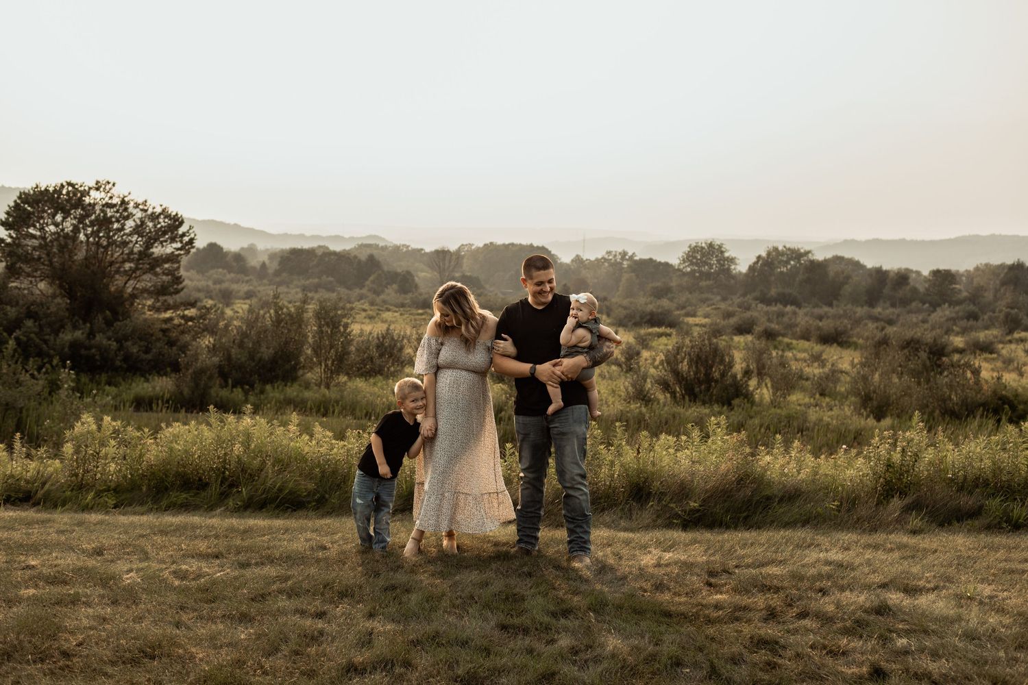 A family of three sharing a tender moment on a hilltop during golden hour.
