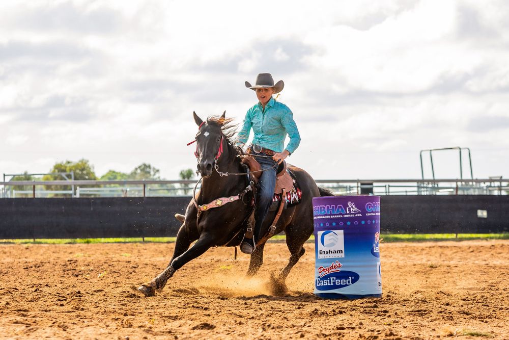 Horse and rider perform barrel racing pattern in dusty arena.