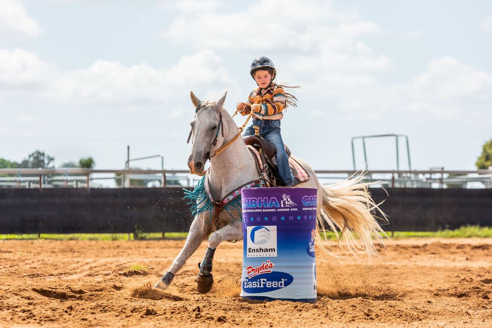 Horse and rider navigating around blue barrel in arena competition.