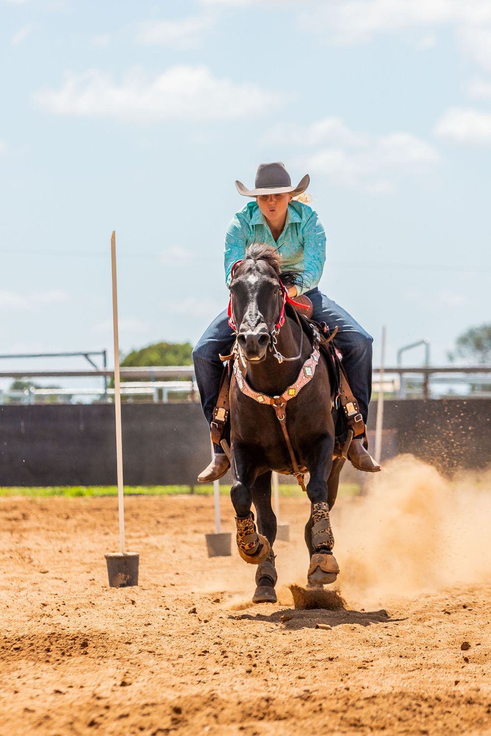 Horse and rider kick up dust while racing around arena obstacles.