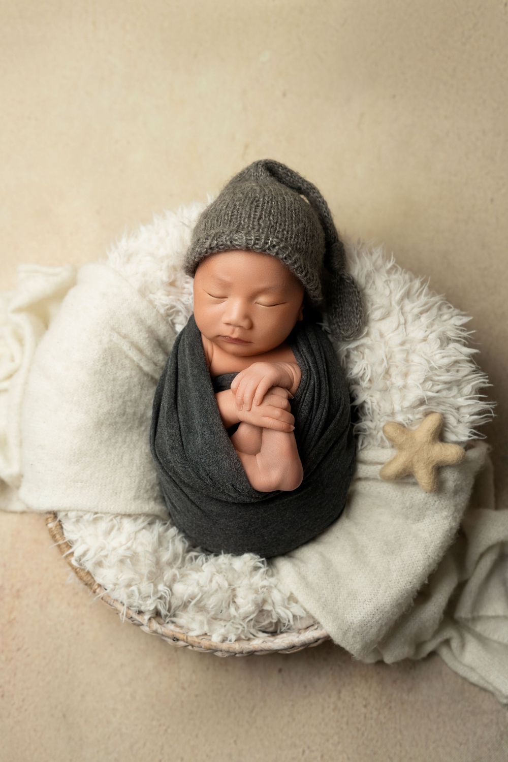 Sleeping newborn wrapped in gray fabric wearing knit hat lying on white furry blanket with starfish decoration.
