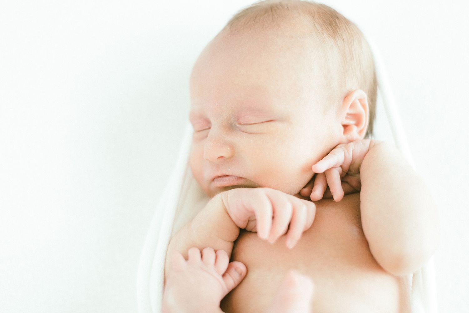 Peaceful close-up portrait of sleeping newborn baby in white.