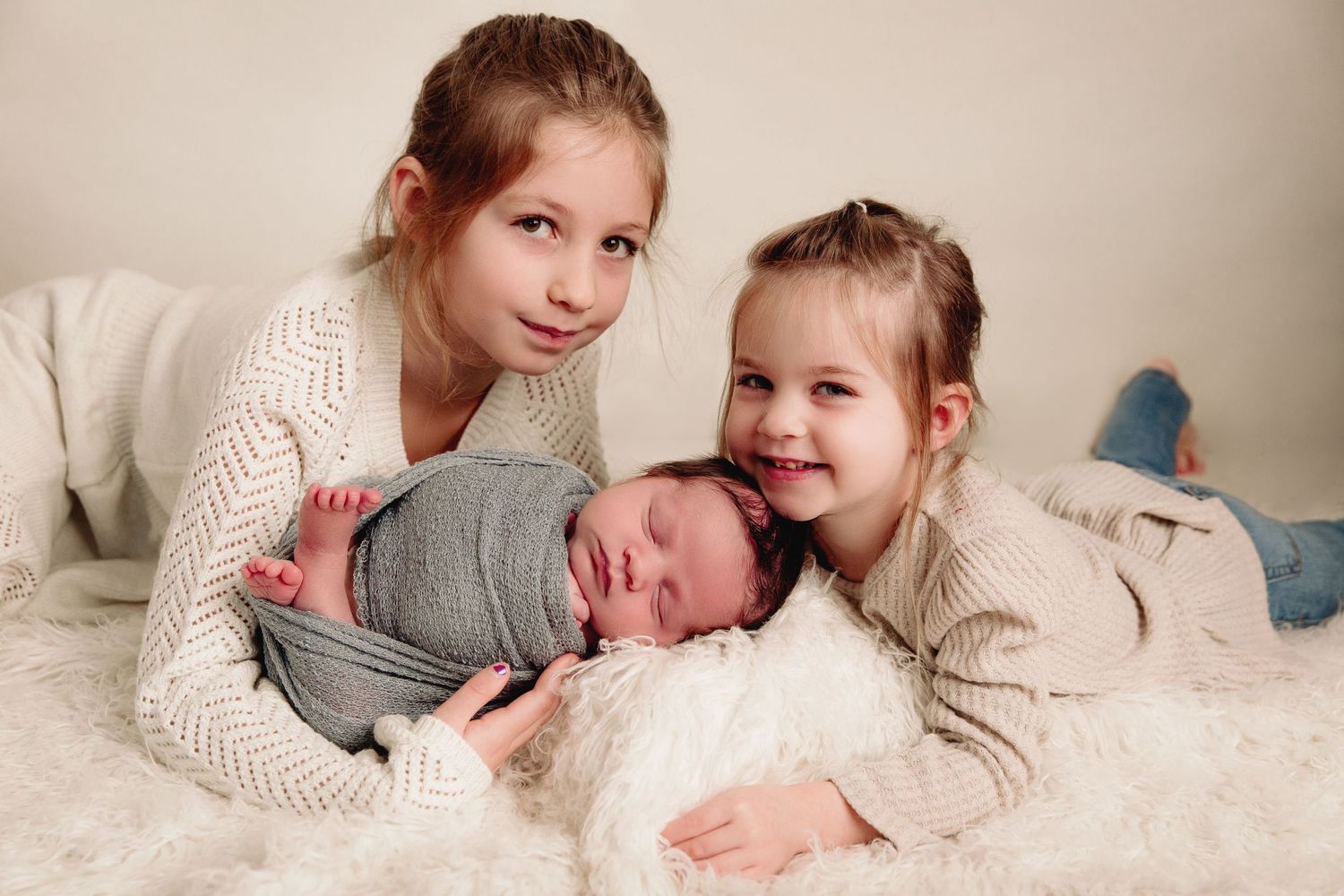 two older siblings laying with baby boy on white fur
