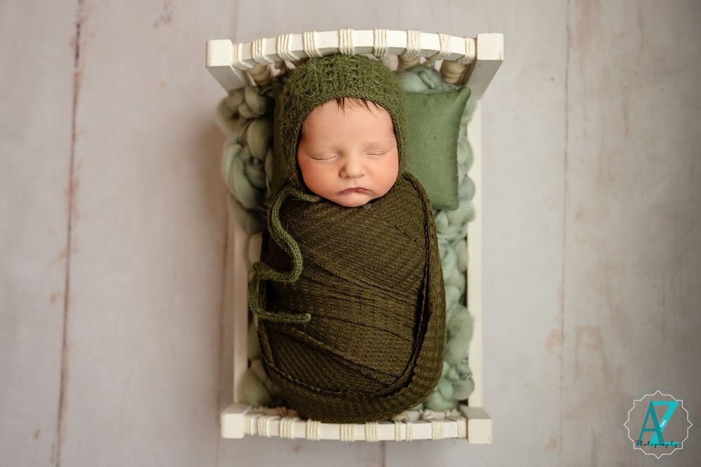 Sleeping newborn wrapped in green swaddle resting in white wooden crate.