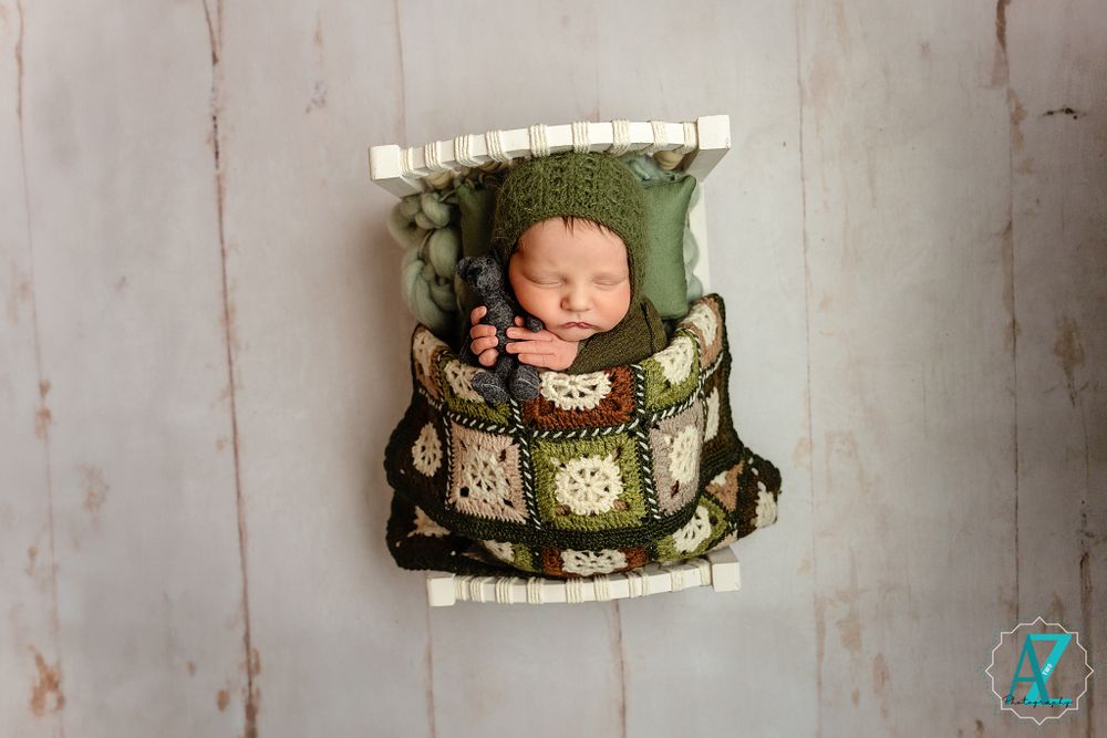 Sleeping baby nestled in decorated crate with green and white patchwork quilt.