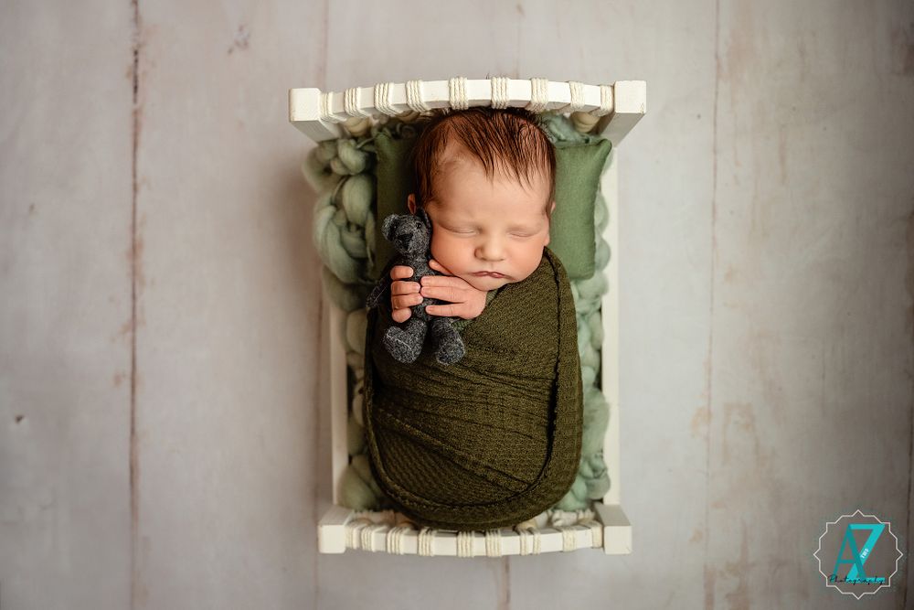Newborn sleeping peacefully in a rustic white crate lined with sage green fabric.