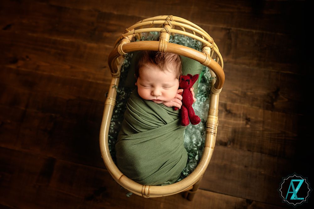 Sleeping newborn wrapped in green fabric inside a woven basket with textured bedding.