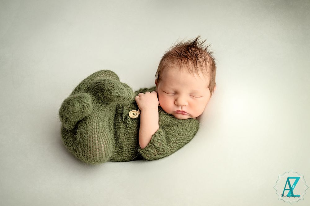 Sleeping newborn in cozy green knit wrap on white background.