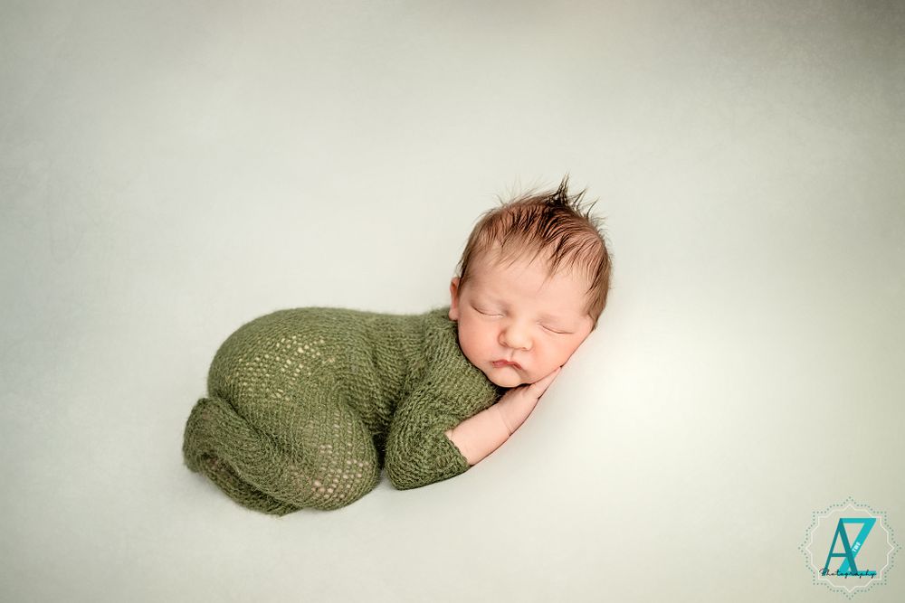 Sleeping newborn wearing sage green knit outfit on light background.