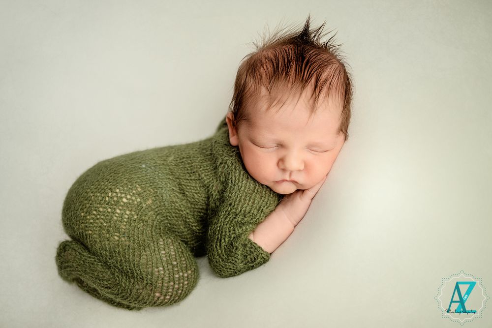 Peaceful newborn in textured green knit outfit against light background.