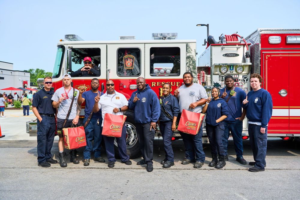 A group of firefighters in uniform gather around their fire truck for a group photo.