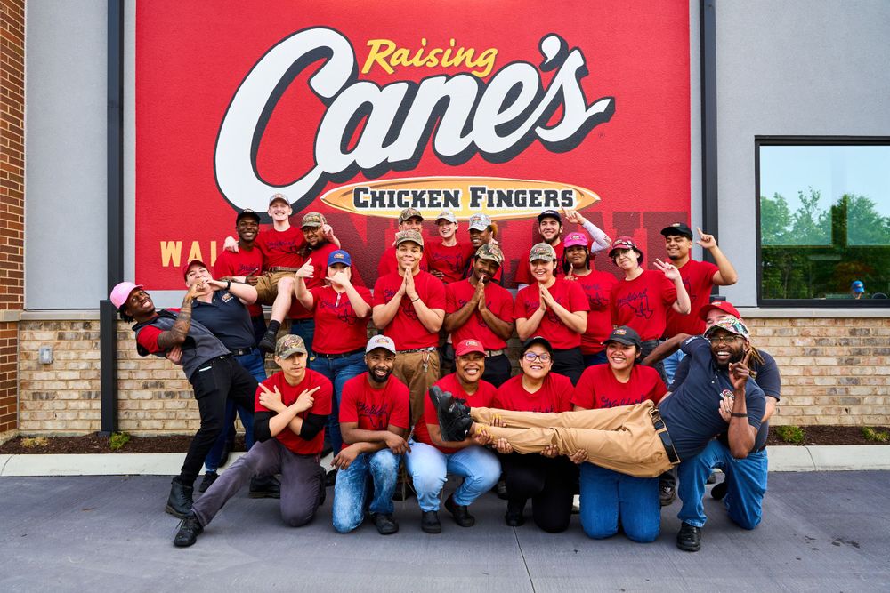 Team members in red uniforms gather for group photo outside Raising Cane's restaurant.