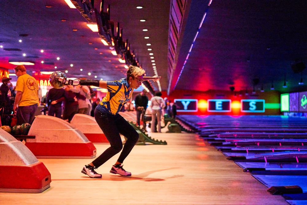 Person bowling in a neon-lit bowling alley with vibrant multicolored lighting.