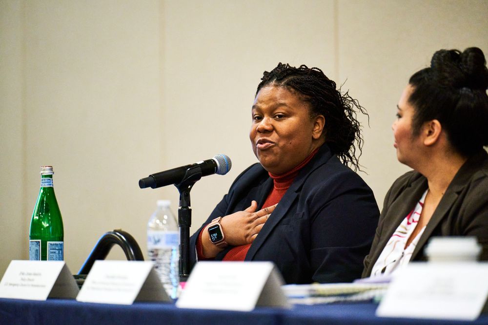 Speaker addressing audience at conference panel with microphone.