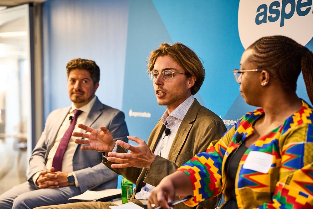 Panel discussion with three speakers at Aspen Institute event against blue backdrop.
