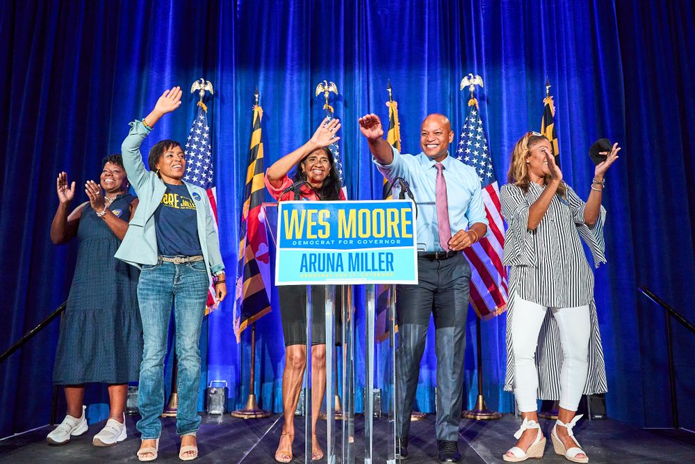 Supporters celebrate on stage at a campaign rally with American flags in the background.
